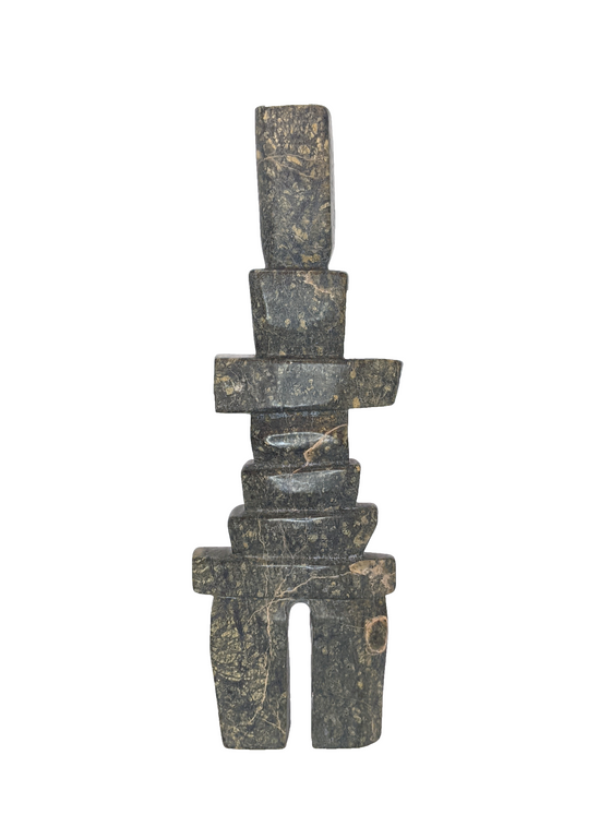 A tall, rigid inukshuk composed of stark, straight lines. Six slabs in varying lengths make up the body, with the legs and head being very tall by comparison. The stone is striking brown and green.