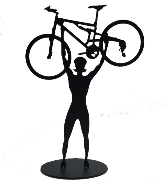 This metal sculpture shows the matte black silhouette a female cyclist facing the viewer. She holds a mountain bike triumphantly above her head. The bike design is slightly simplified, and the wheels have no spokes. The piece stands on a small oval base.