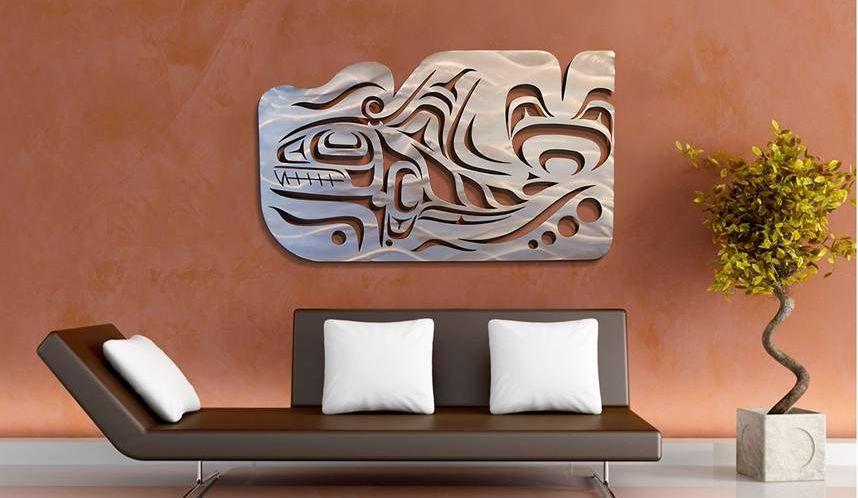 A Coastal Salish Orca wall sculpture hung on a wall. The large sculpture is two thirds as long as the couch beneath it.
