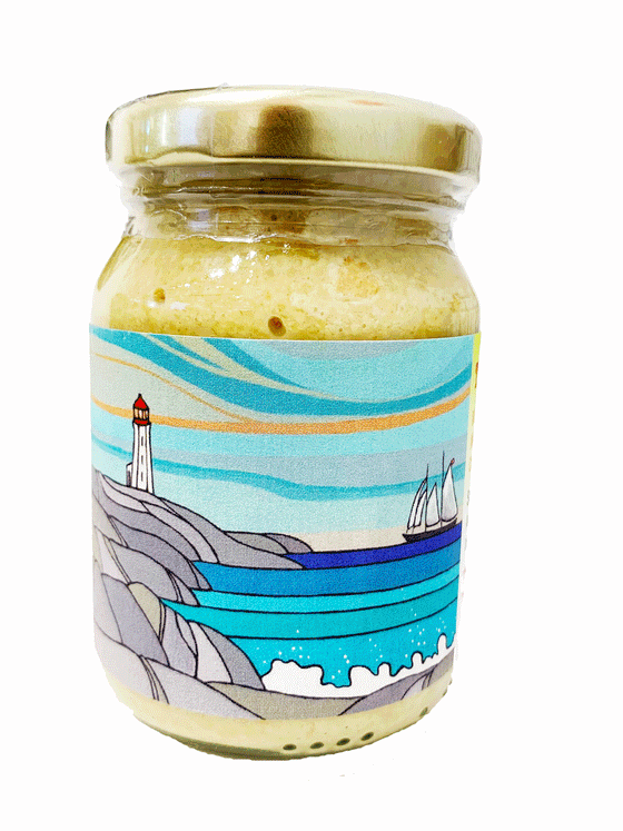 Clear jar with light yellow mustard inside. Label depicts Nova Scotia artist Sabine Kearns' "Into the Breeze" - a scene featuring a light blue sky, a lighthouse on grey rocks, and a blue ocean with a ship.