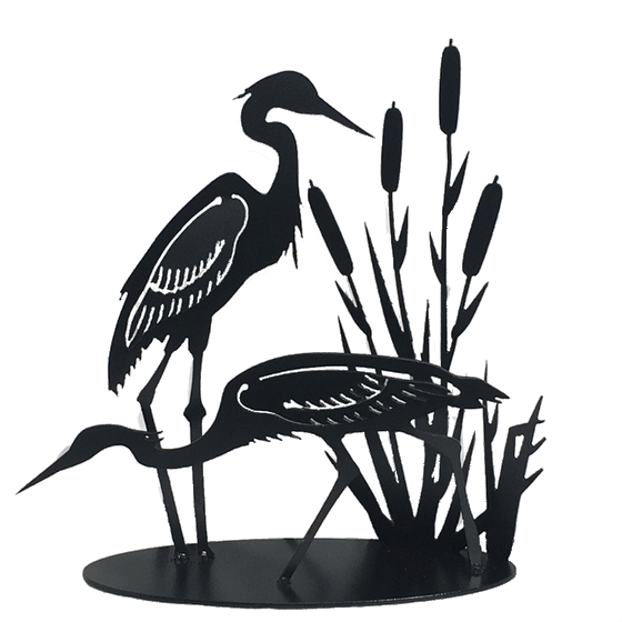 This metal sculpture shows the matte black silhouette of two herons standing with cattails. The left heron stands upright, while the right heron is leaning forward to look in the water. The wings of the herons have been partially punched out of the metal, and bent to render the birds in 3D. Individual wing feathers are visible. The cattails are cut very delicately and in lifelike shape and proportion to the herons. The piece sits on a long oval base.