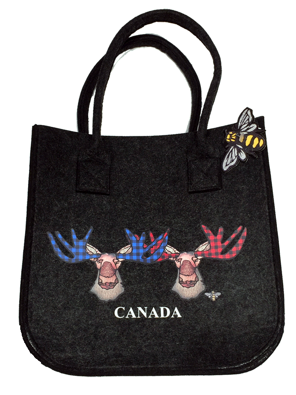 This small dark grey felt bag has two overhead handles and features an art print of two moose. The left moose’s antlers are coloured with blue buffalo check, while the right moose has red buffalo check. The moose’s ear, nose, face and neck are all coloured with different shades of brown. Underneath the moose the word Canada has been written in white text. At the bottom right of the picture is the artists mark—a small picture of a bee.