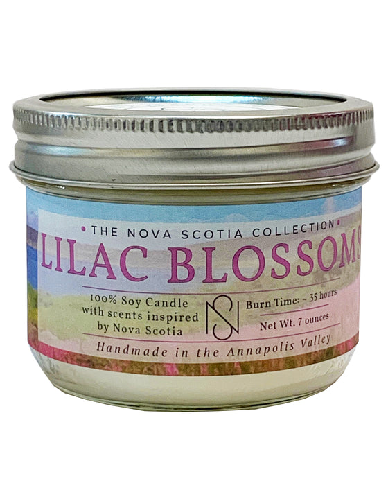 Cylindrical candle Jar with a tin cap. There is a label on the candle Jar, with a flower field background, and Lilac Blossoms written in the middle.
