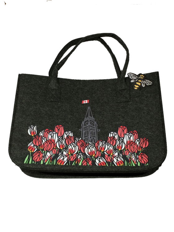 This large dark grey felt bag has two overhead handles and features an art print of the peace tower and a field of tulips. The peace tower is in the center of the picture and is flying the Canadian flag. The dense field of flowers has red tulips and Canada 150 tulips, which are white with fiery streaks of red. The line work gives the tulips an impression of stained glass.