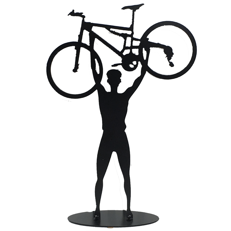 This metal sculpture shows the matte black silhouette a male cyclist facing the viewer. He holds a mountain bike triumphantly above his head. The bike design is slightly simplified, and the wheels have no spokes. The piece stands on a small oval base.