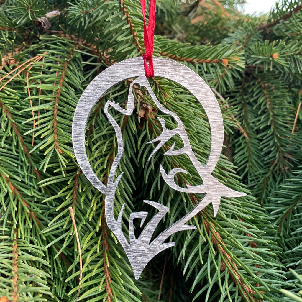 The wolf ornament with a red ribbon attached and hanging on a pine tree. 