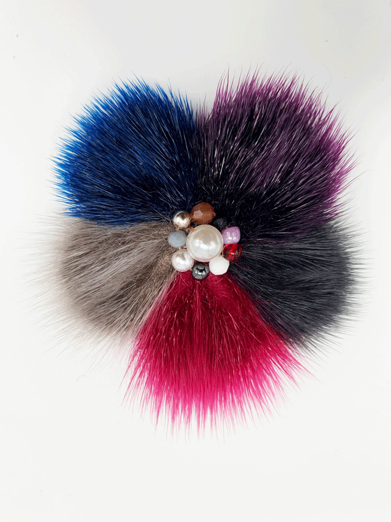 sealskin in the shape of a multicolored flower, with many pearl like balls in the center. The flower is mixtures of blue, dark purple, pink, and light and Dark grey.