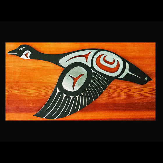 A Canada goose in flight done in Haida style. The brushed steel base provides brilliant contrast to the black powder-coated top layer, creating a dazzling, textured piece of wall art. This goose has its wings down.