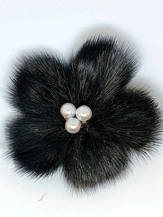 sealskin in the shape of a black flower, with three white pearl like balls in the center.
