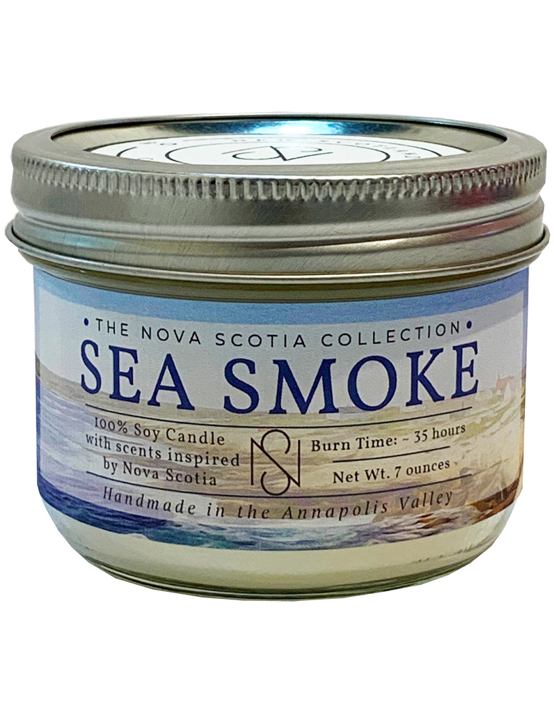 Cylindrical candle Jar with a tin cap. There is a label on the candle Jar, with a ocean background, and Sea Smoke written in the middle.