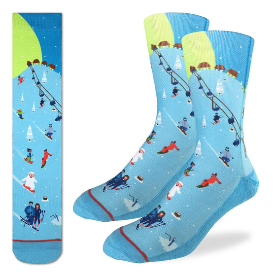 These fun socks feature a cartoon image of a ski slope with people riding a lift, people skiing or snowboarding down the hill, and some shacks at the top of the hill with snow covered pine trees dotted around the slope. The slope is coloured a light blue, while the sky behind is a darker blue with the moon and stars. The sole, toe, and heel of the socks are a darker blue, same as the sky. The active fit socks sport elastic arch bands to contour to your feet and provide support.