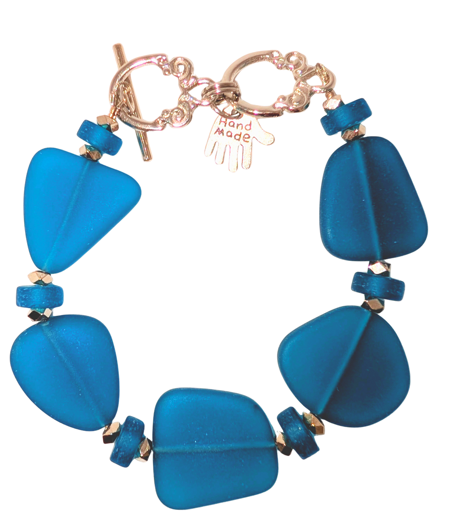 Bracelet with navy sea glass, beads, and a small hand charm that says "handmade" between 2 rings for sizing. The clasp is a silver toggle clasp.