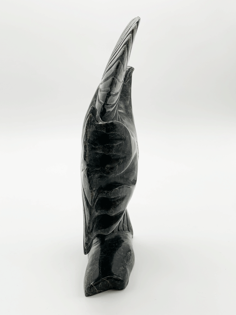 A black owl stands with wings pointing straight up, as if about to take off into flight. This image shows the eagle's feet and the detailed carving that shapes the feet and feathers.