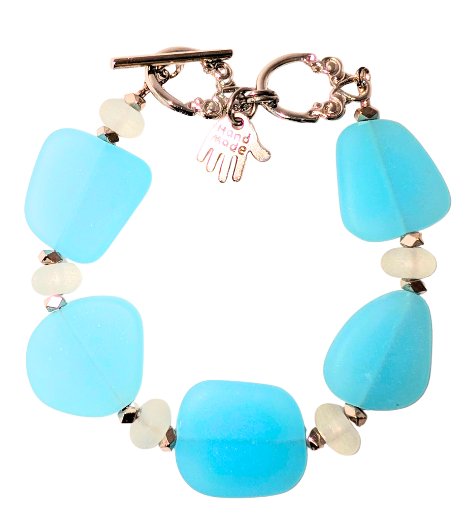 Bracelet with light blue sea glass, white beads, and a small hand charm that says "handmade" between 2 rings for sizing. The clasp is a silver toggle clasp.