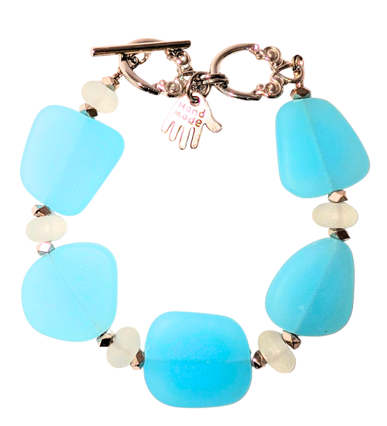 Bracelet with light blue sea glass, white beads, and a small hand charm that says "handmade" between 2 rings for sizing. The clasp is a silver toggle clasp.