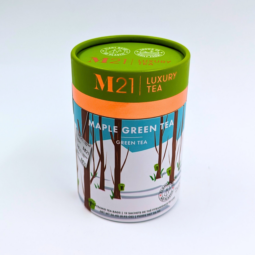A cylindrical box that holds twelve maple green flavoured tea bags. The tea bags are pyramid shaped and are blended and packed in Canada. The container is made from 100% recycled paper. The illustration on the canister depicts a forest scene with maple trees. Small green buckets hang from the trees representing the maple syrup harvest. The green in the imagery matches the green coloured lid. It includes instructions to brew for three to five minutes. 