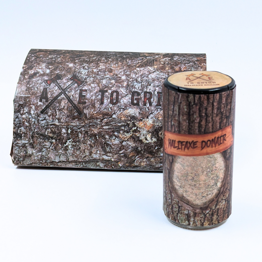 This spice blend is packaged in a reusable/recyclable glass jar printed to look like a log of firewood. The spice mixture is visible through a clear window in the packaging. Larger packaging  with "Axe To Grind" logo on box that looks like firewood.