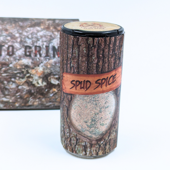 This spice blend is packaged in a reusable/recyclable glass jar printed to look like a log of firewood. The spice mixture is visible through a clear window in the packaging.