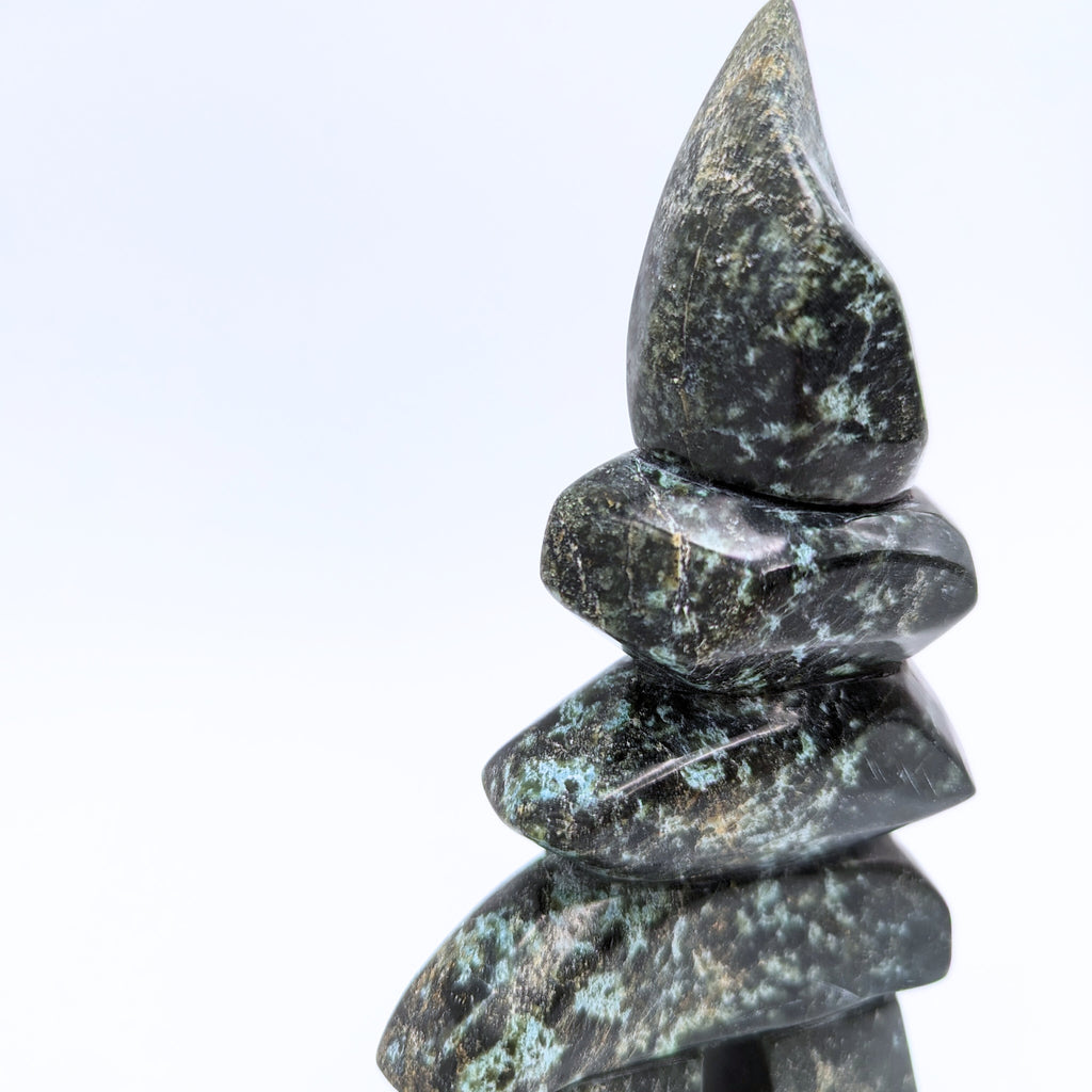 An inukshuk made of four single stones stacked on two legs. The shape very strongly suggests a person shape. The stone is brilliantly mottled green, brown, and black.