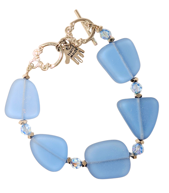 Bracelet with periwinkle sea glass, beads, and a small hand charm that says "handmade" between 2 rings for sizing. The clasp is a silver toggle clasp.