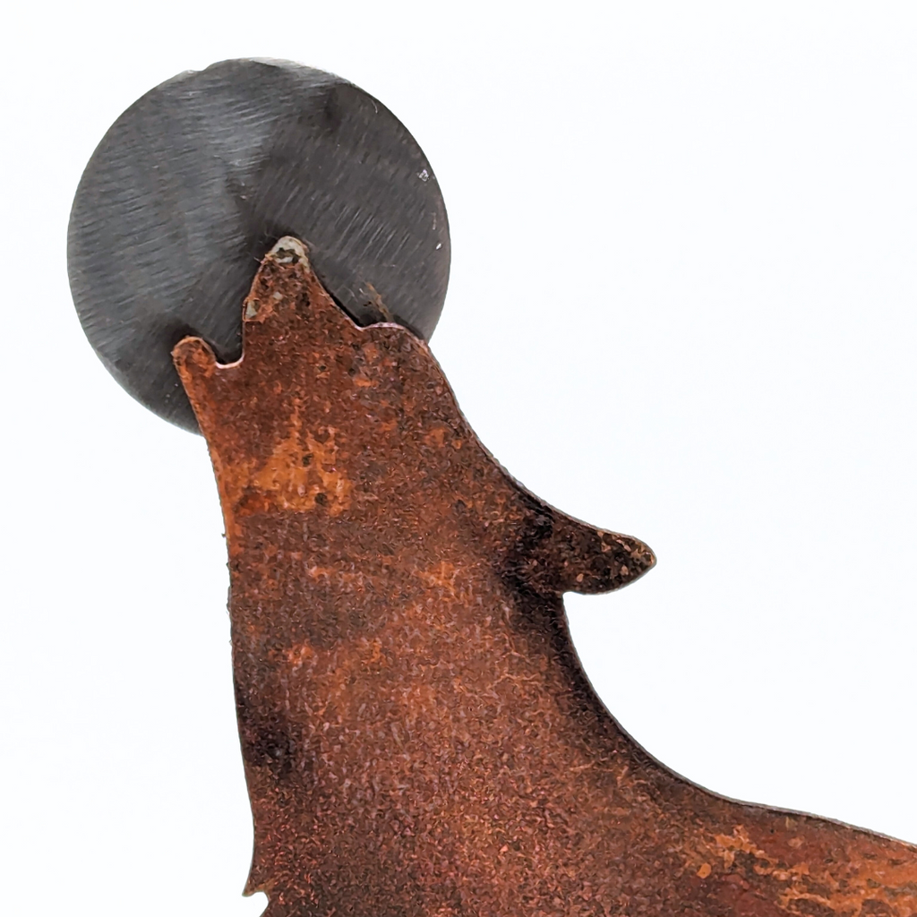 a close up of a weathered looking metal wolf art howling at a silver moon circling the wolfs head.