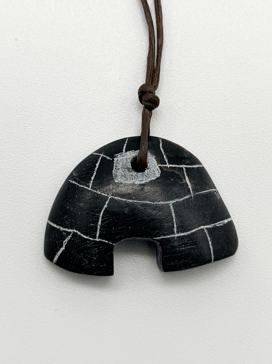 A black igloo pendant with white lines to outline snow blocks. The entrance of the igloo is cut out. The top of the igloo has a white circle where the black necklace thread goes through.