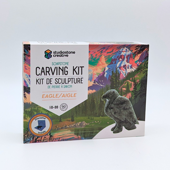 The box shows the green stone eagle of the carving kit against a beauftil and colourful backdrop of a mountain and forest scene, overlooking a tranquil lake.