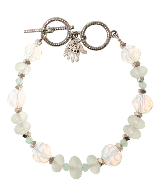 Bracelet with white sea glass, beads, and a small hand charm that says "handmade" between 2 rings for sizing. The clasp is a silver toggle clasp.