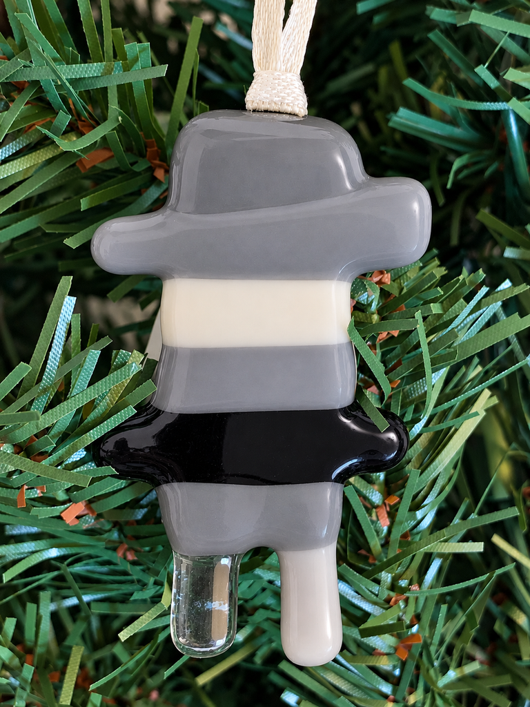 A fused glass Inukshuk ornament with gray, white, and black colors predominantly visible.