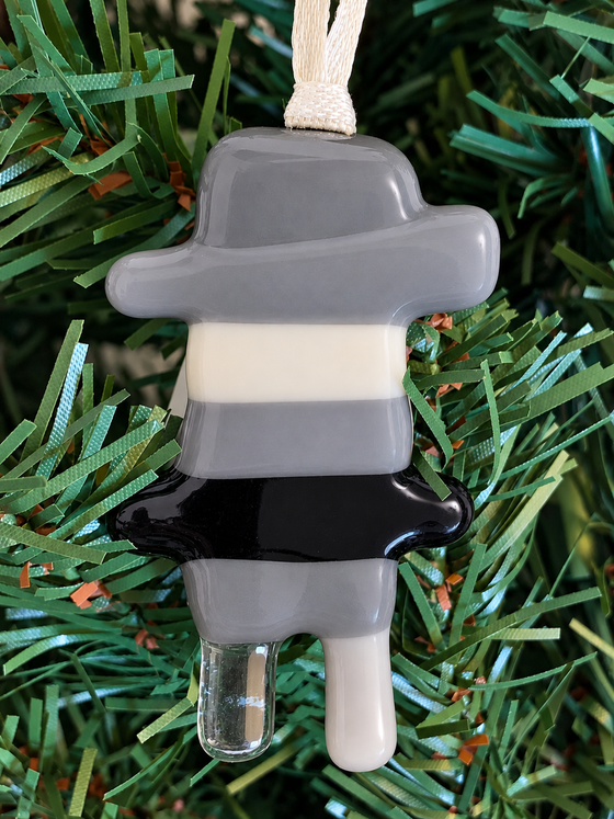 A fused glass Inukshuk ornament with gray, white, and black colors predominantly visible.