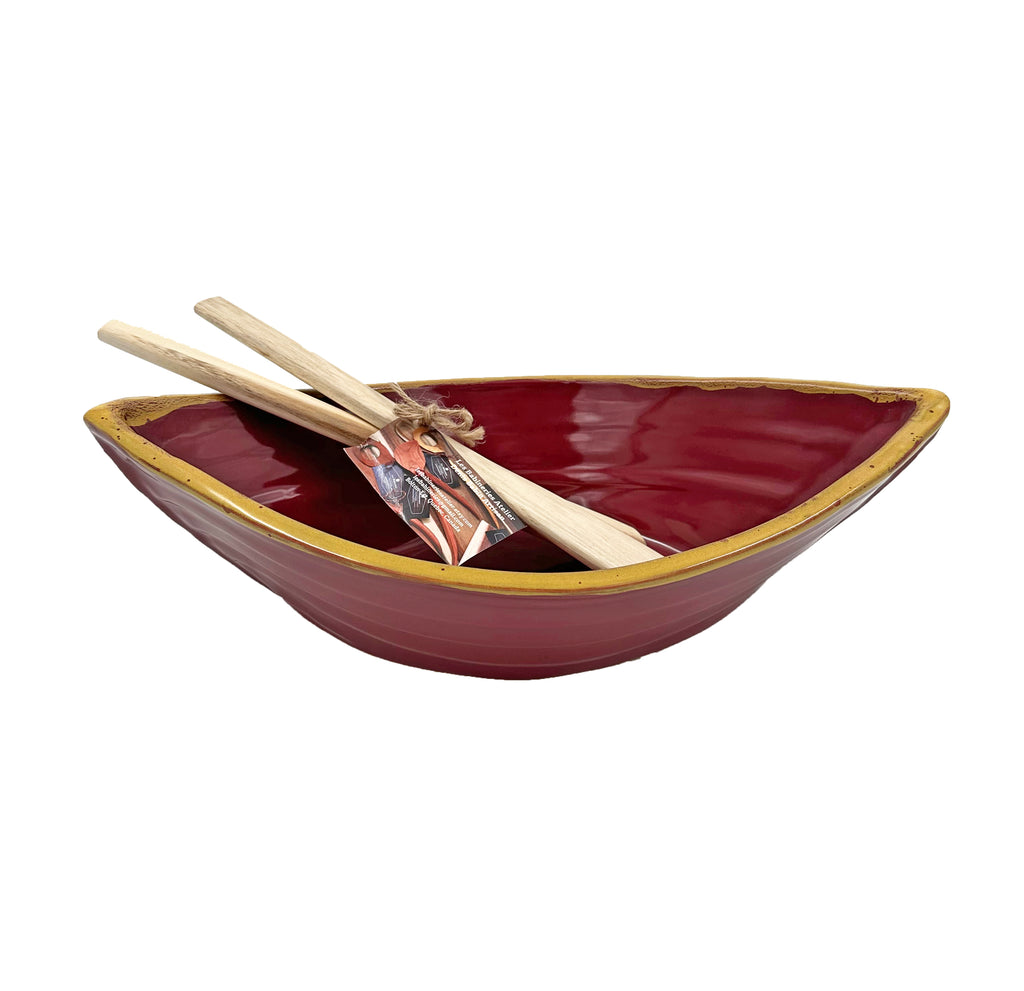 Bowl is red with a yellow rim on the top edges. Bowl is oval shaped with points at two opposite ends. Two wooden paddles sitting inside the bowl.