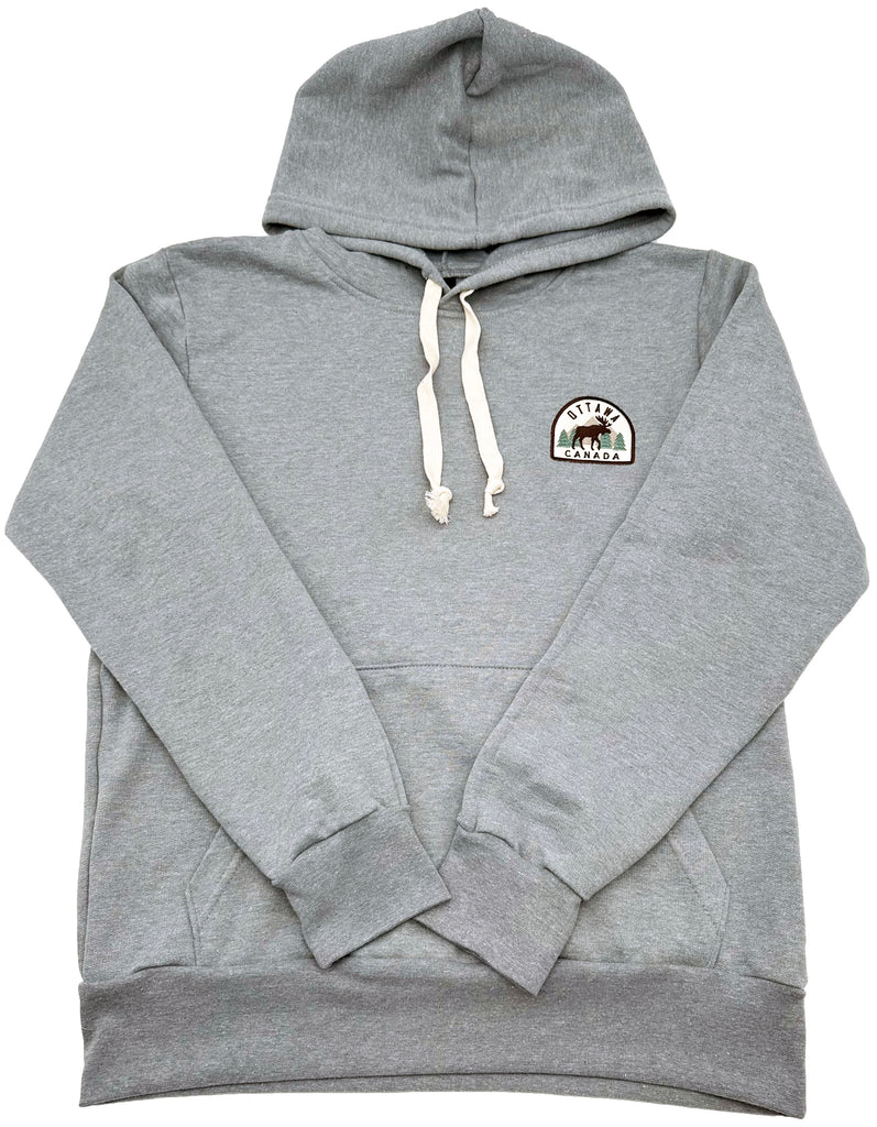 Grey hoodie with white drawstrings. On the top right corner there is a semi-circle patch. It is outlined in brown and has a light beige colour inside. The words Canada are on the bottom on the straight half of the circle. Ottawa is curved at the top of the circle. There is a dark beige mountain with green trees on both sides. In the front is a brown moose.