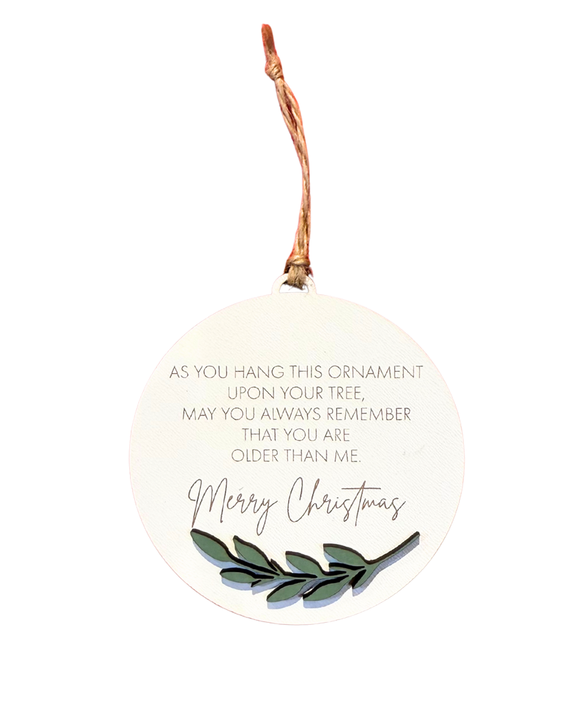 Round Christmas ornament with text that reads 'As you hang this ornament upon your tree, may you always remember that you are older than me' and 'Merry Christmas' underneath in a larger font.