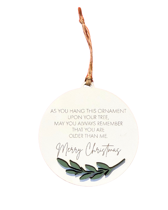 Round Christmas ornament with text that reads 'As you hang this ornament upon your tree, may you always remember that you are older than me' and 'Merry Christmas' underneath in a larger font.