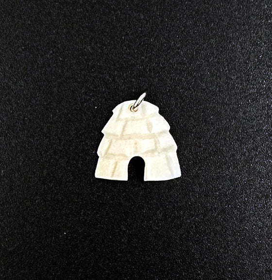 An off-white igloo pendant. The snowblocks are indented and create texture, and the entrance of the igloo is cut out. A small silver hook goes through a hole at the top of the igloo.