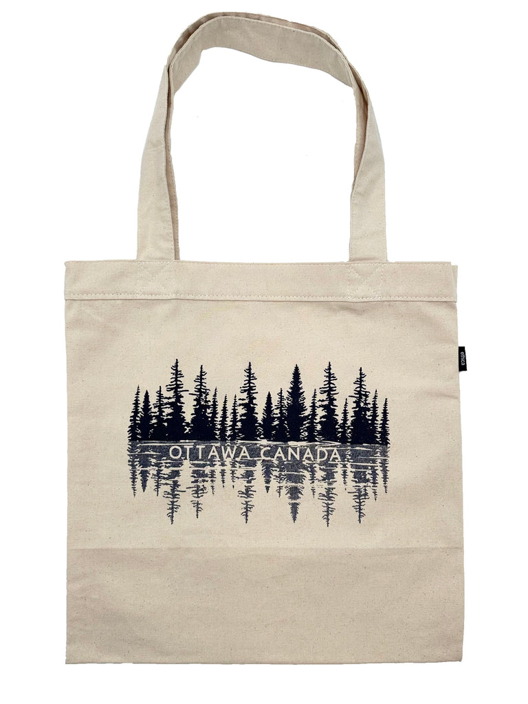 A light beige square tote bag with two handles at the top. Has a grain effect with black trees and a grey reflection of the trees underneath. In the reflection is also written Ottawa Canada in all caps.