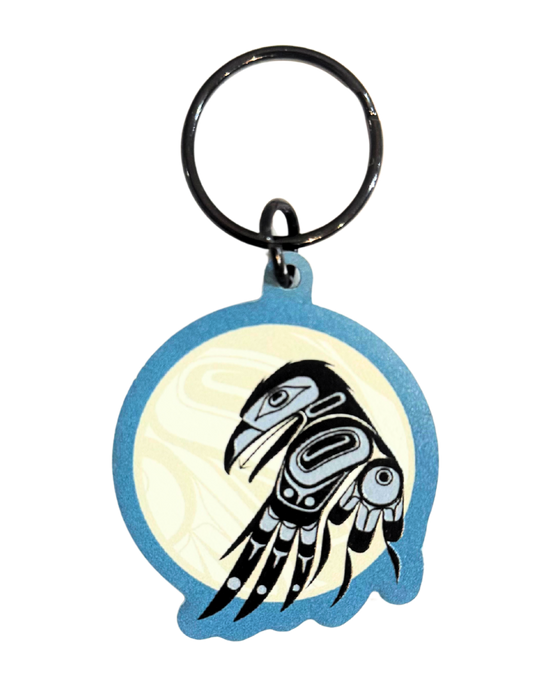 Keychain with an indigenous style raven infront of a moon. The raven is black and light grey. The moon is a pale yellowish white with a blue outline.