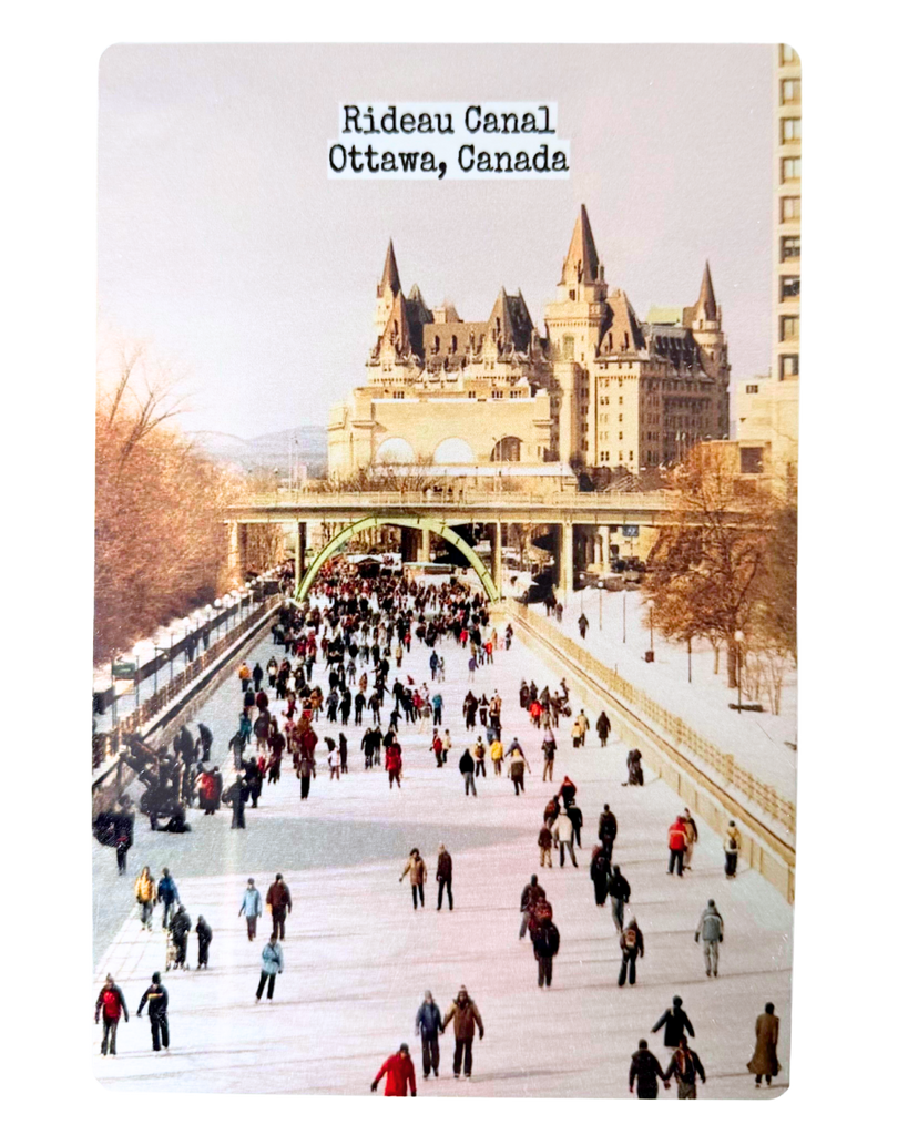 A metal postcard with an image of the Rideau canal skateway and Chateau Laurier in the background.