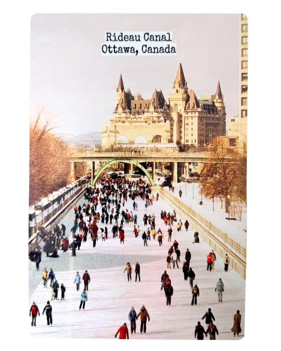 A metal postcard with an image of the Rideau canal skateway and Chateau Laurier in the background.