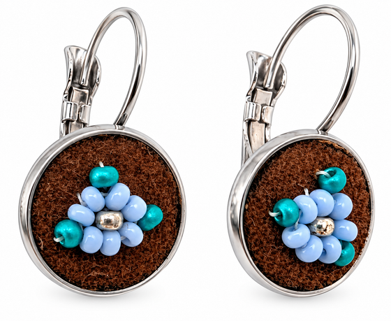 A pair of silver leverback earrings with round brown moose hide facepalm charms featuring blue and silver beaded flower details, shown on a white background.