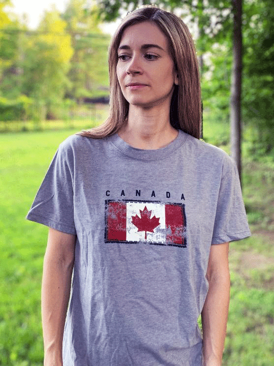 A grey shirt. In the middle is a worn looking canadian flag with a black outline. On top is written in black "Canada".
