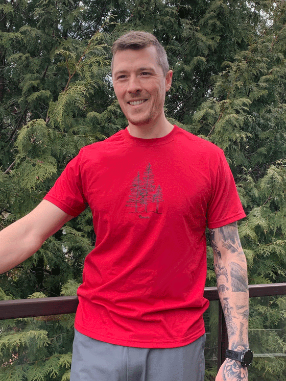 A red shirt. In the center is a black line design of three trees. Underneath in small cursive letters is written "Canada".