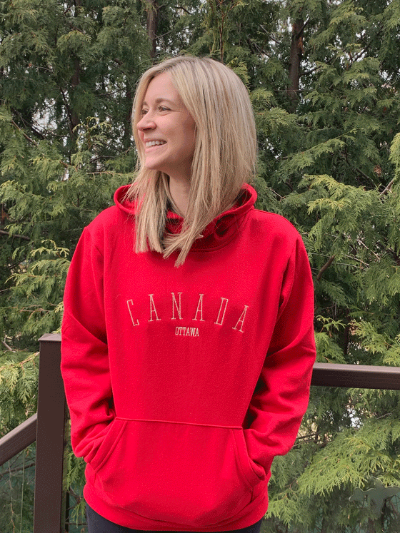 A red hoodie with Canada written in a thin white text across the chest. Ottawa is written below in a smaller version of the same font.
