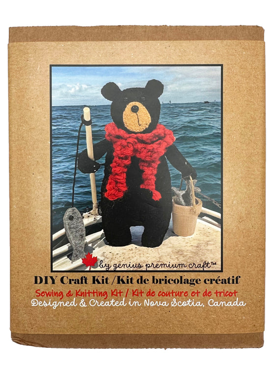 A handmade felted black bear stands holding a fishing rod, complete with felt fish, in one hand, and a bucket with more fish in the other. The bear wears a chunky knitted red scarf.