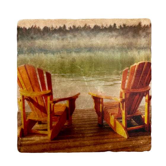 Two wooden Muskoka chairs sit on a weathered dock overlooking a lake. Mist rises off the lake, partially obscuring the dark trees on the other side.
