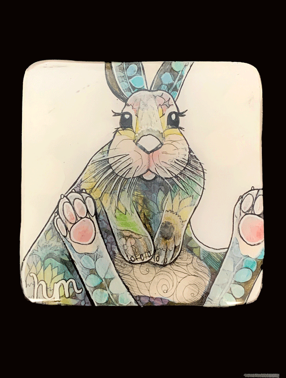 A grey, yellow, green, blue, and pink rabbit covered in an assortment of flower and leaf-shaped patterns is sitting with both feet up. A white background is behind the rabbit.