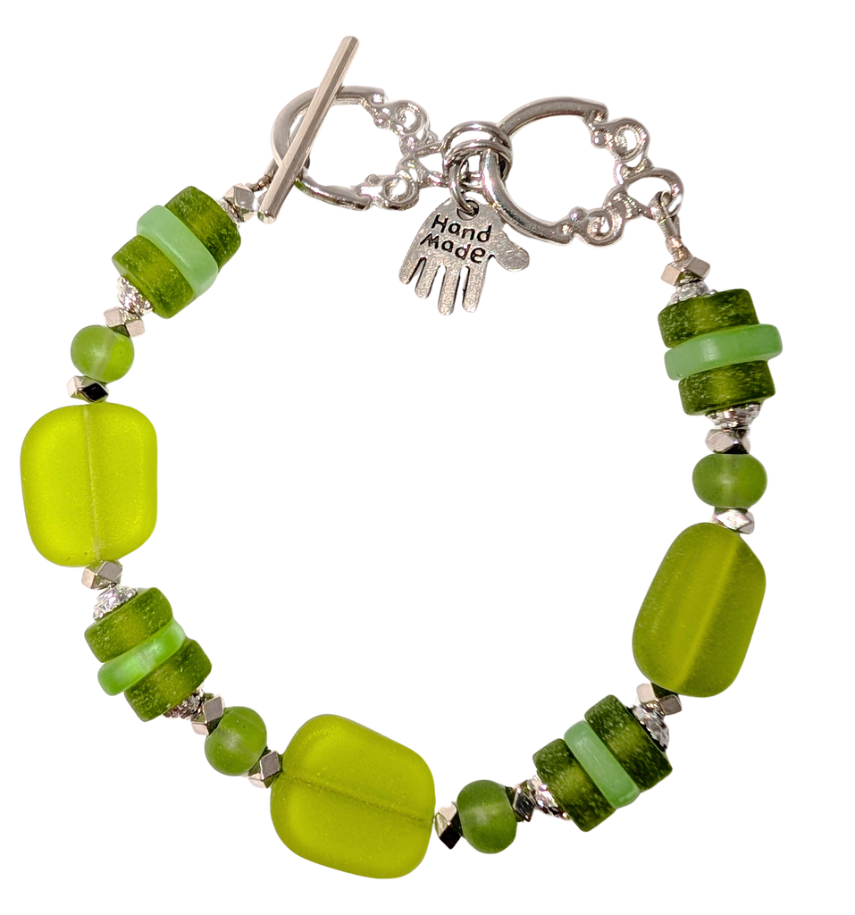Bracelet with green sea glass, beads, and a small hand charm that says "handmade" between 2 rings for sizing. The clasp is a silver toggle clasp.