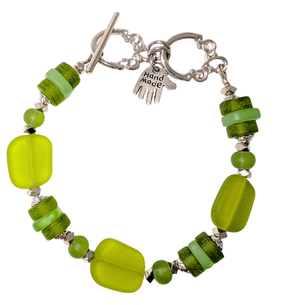 Bracelet with green sea glass, beads, and a small hand charm that says "handmade" between 2 rings for sizing. The clasp is a silver toggle clasp.
