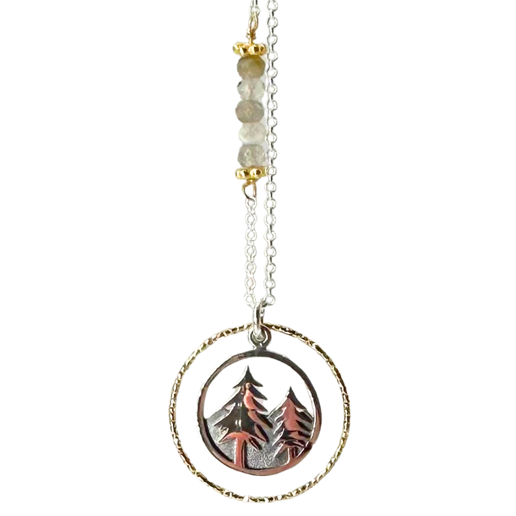 Silver chain with four coloured beads in middle of chain attached with gold chain links that look like flowers. Pendent is a gold ring that has triangle ridges. Silver ring in the middle that has pine trees in the front and mountains in the back.