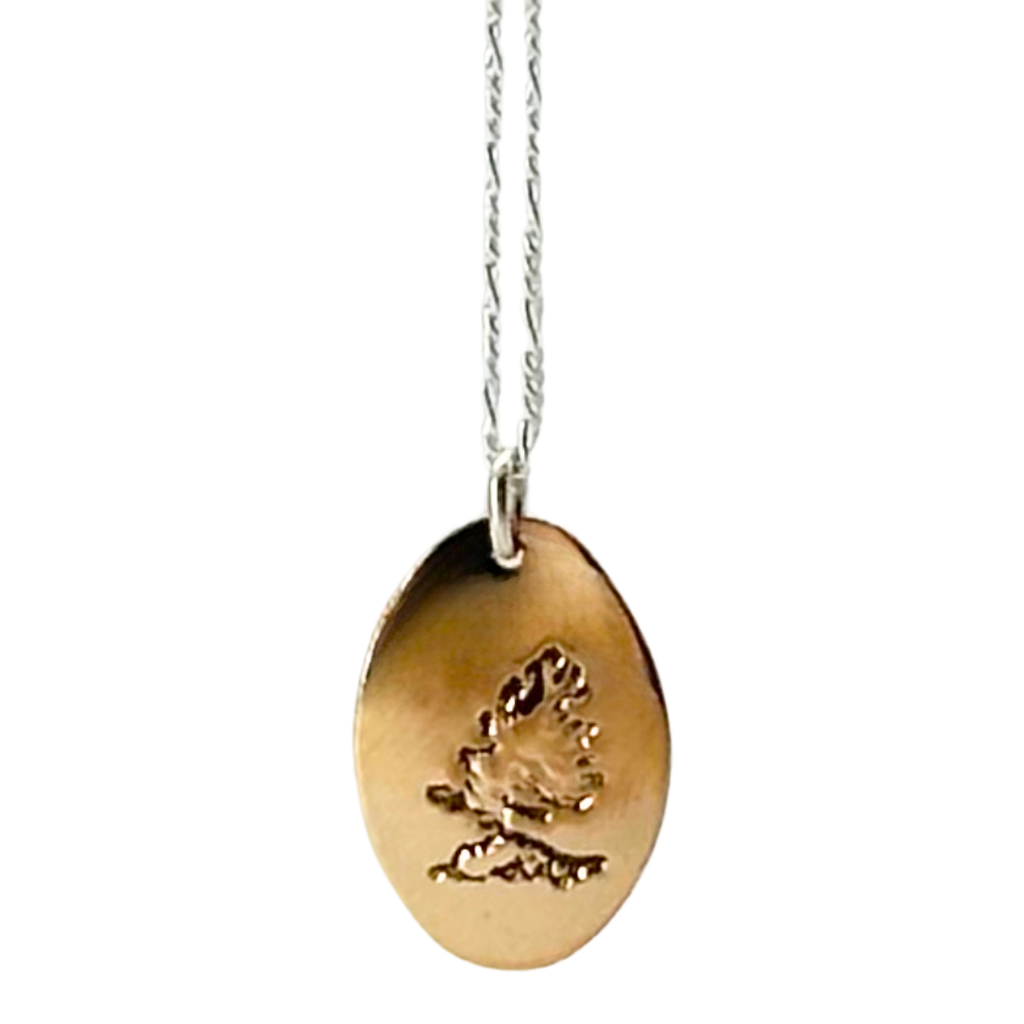 A necklace made of 14 karat gold fill and sterling silver on a gold chain. The base is an oval of bright gold with a rugged windswept pine on rock etched into the center.